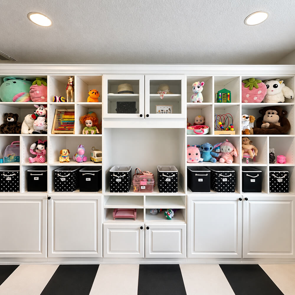 Fully organized kids' playroom in Las Vegas by Lifelystyle — large white built-in shelving unit with labeled black polka-dot bins, curated toy display, and black-and-white striped floor