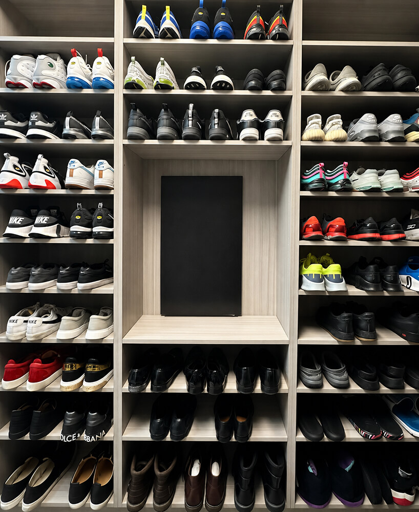 Floor-to-ceiling sneaker wall organized by Lifelystyle in Las Vegas — hundreds of pairs displayed on custom light-wood shelving with a centered display niche for a collector's boutique experience at home